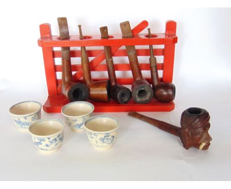 A collection of pipes on a pipe rack in the form of a painted red gate to include a carved pipe in the form of a man's head w