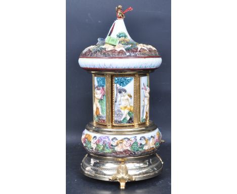 Capodimonte - A vintage late 20th century porcelain and brass musical carousel cigarette dispenser having a putti finial with