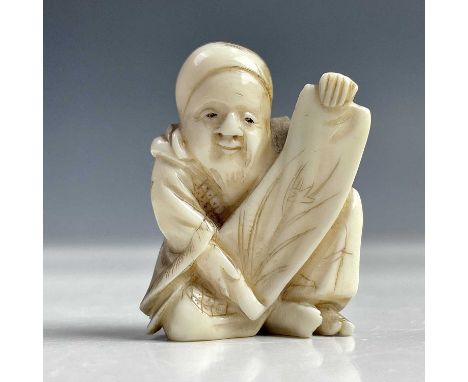 A Japanese netsuke of a seated man holding a scroll, Meiji period, circa 1890, height 3.5cm, width 3cm.