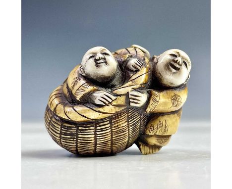 A Japanese ivory netsuke of two figures and a basket, Meiji period, height 3.5cm, width 4.5cm.