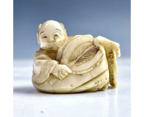 A Japanese ivory netsuke of a boy holding a palm leaf fan, Meiji period, height 2.7cm, width 3.4cm.