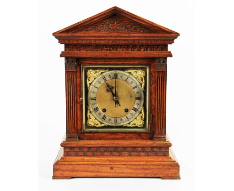 A carved oak mantel clock with column design with patterned top, the face having brass spandrels with silvered chapter ring w