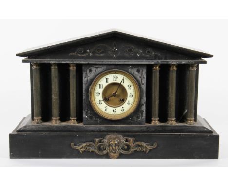 An early 20th Century American style black slate clock with column design with ornate scroll decoration with mask design to f