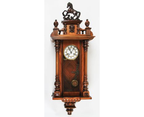 An early 20th Century mahogany vienna wall clock with carved finials and columns with rearing horse top, the dial having whit