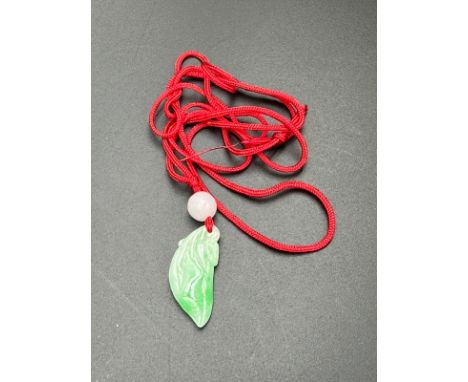 A jade pendant on a red string necklace.