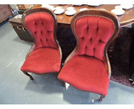 A pair of Victorian style button-upholstered nursing chairs, covered in red fabric and raised on cabriole legs. 