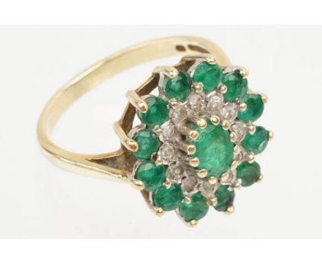 9ct gold, emerald and diamond cluster ring. The ring being set with a central oval cut emerald surrounded by round cut emeral