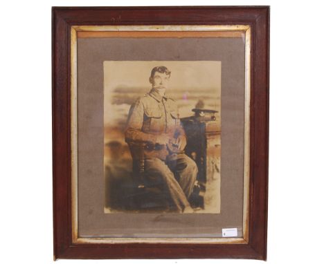 A large WWI First World War framed and glazed photograph of a soldier. Depicted sitting, with cap and pipe on plinth next to 