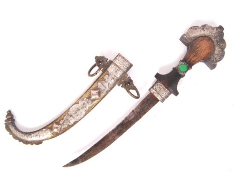 An early 20th century Middle Eastern Jambiy a dagger having a wooden carved, brass adorned and gem handled curved edge bladed