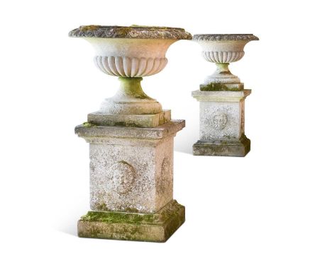 A pair of re-constituted stone Campana urns on plinths, the moulded rims over part gadrooned bodies, on rectangular plinth ba