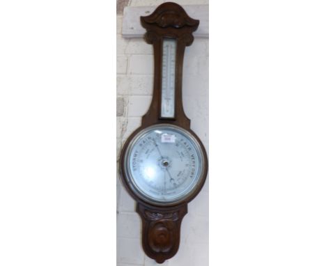 An Edwardian carved oak aneroid barometer with thermometer