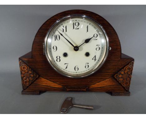 AN oak cased mantel clock with carved decoration, Arabic numerals to the dial, with key and pendulum.