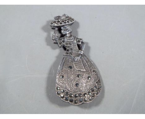 A white metal extremely detailed  brooch set with marcasite depicting a Lady carrying fruit basket, marked verso EXTRA [pleas