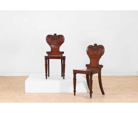 A pair of William IV mahogany hall chairs, c.1835, each with carved scrolling foliate decoration to the back, a square seat, 