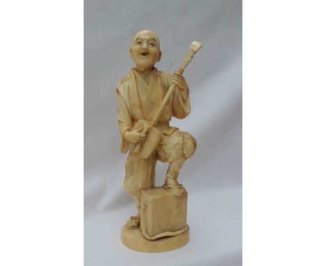 A 19th century Japanese carved ivory figure group of a man playing a musical instrument, his foot resting on a box, with a ci