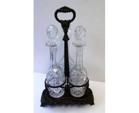 An electroplated on copper three decanter tantalus with a C scrolling and leaf applied loop handle, the trefoil base with scr