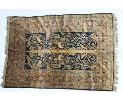 A silk rug with a central panel with a blue ground with a central tree trunk with monkeys, serpents, lions, deer, peacocks an