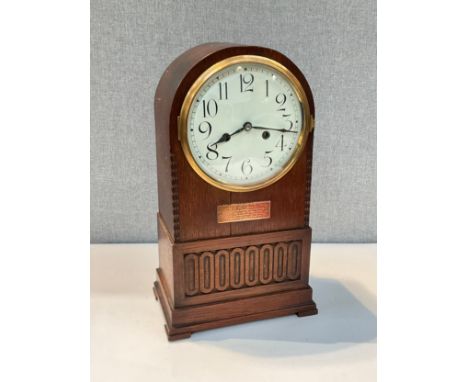 An early 20th Century oak cased mantel clock of arched form, Arabic enamel dial, with 1912 dated plaque, carved detail, foote