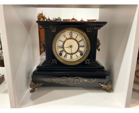 An early 20th Century black painted metal mantel clock, Roman dial, lion mask ring handles, gilt enriched scrolled detail, wi