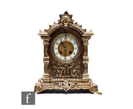 An early 20th Century brass mantle clock, the eight day striking movement enclosed by a circular glazed door, lion mask pedim