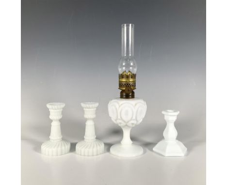 A set of four milk glass items, including one lamp with a bronze head featuring abstract circle art, two identical candlestic
