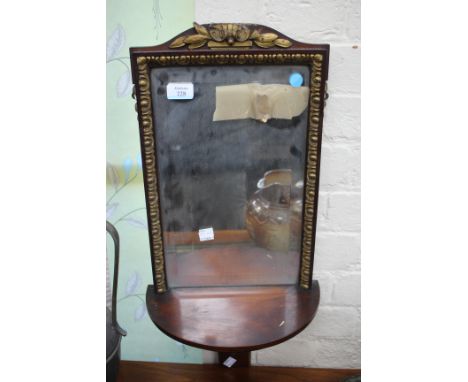 A MAHOGANY AND PARCEL GILT FRAMED HANGING WALL MIRROR with D shaped shelf supported on a gilt bracket beneath, 32cm wide x 62