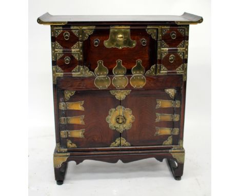A SMALL ORIENTAL SIDE CABINET with brass mounts to the four drawers and three cupboard doors, all with ring handles and stand