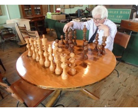 A polished oak circular chess table, on crossed and splayed tripod supports, together with a complete hardwood oversized ches