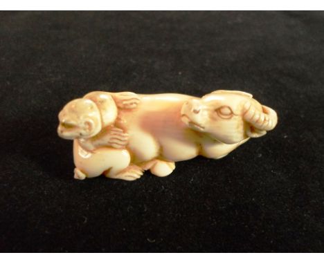 A Meiji period ivory carved netsuke formed as a recumbent buffalo, his head turned to view a monkey on his back, 4.8cm long, 