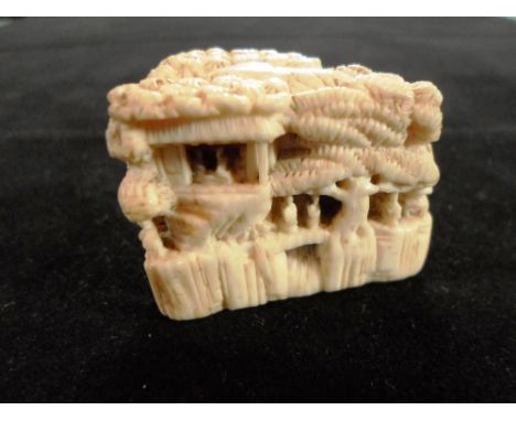 A Meiji period ivory carved netsuke of a triangular shaped house, with figures at the windows below shaped roof, 2.6cm tall, 
