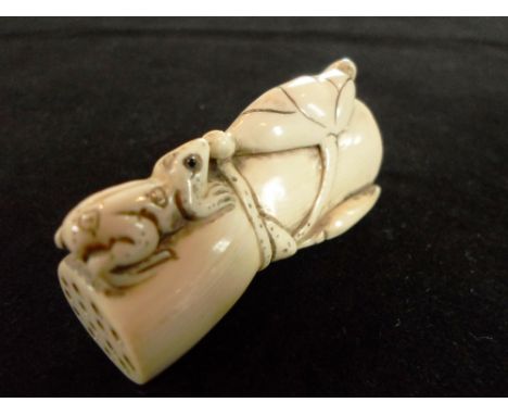 A Meiji period ivory netsuke of a frog with applied eyes, eating a leaf whilst perched on a log, the log having pierced ends,