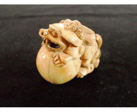 A late 19th century Japanese carved ivory netsuke of a shishi with a large ball, 3cm tall, unsigned