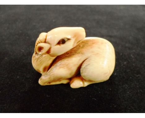 A late 19th century Japanese ivory netsuke of a crouching deer, having  inlaid eyes, his head turned and resting on his back,