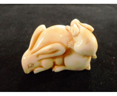 A Japanese ivory netsuke formed of two hares, late 19th century, a smaller one resting on the back of the other, 3cm tall, si