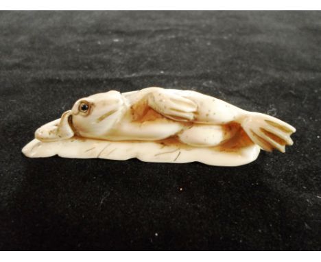 A late 19th century Japanese carved ivory netsuke of a frog, humorously reclining on a flat leaf, 7cm wide, signed