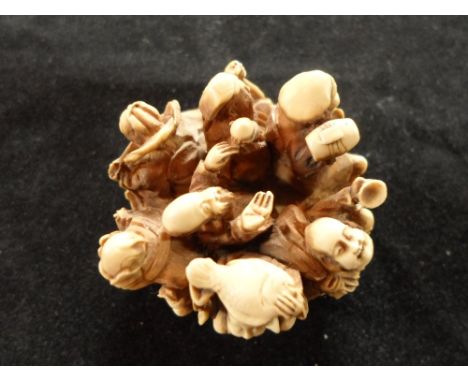 A late 19th century Japanese carved ivory netsuke formed 7 figures, possibly merchants, tightly packed on a circular base, 4c