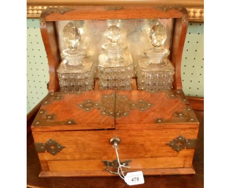 An early 20th century oak three-bottle games tantalus, having four internal glass drinking vessels, playing cards, cribbage b
