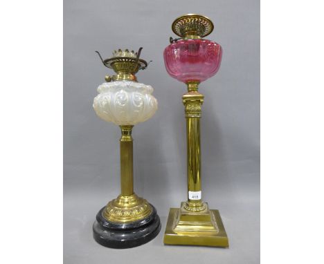 Two brass Corinthian column oil lamp bases, one with a cranberry glass well and the other with an opaque glass well, (2) 
