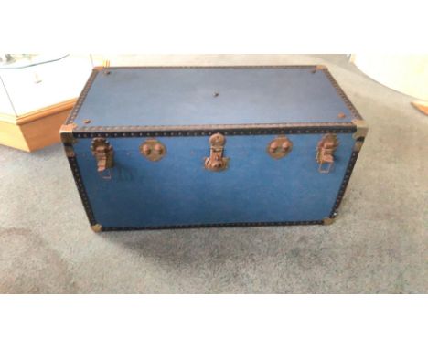 Vintage blue steamer trunk with metal hardware and riveted edges. Features a plaid-lined interior and sturdy latches.