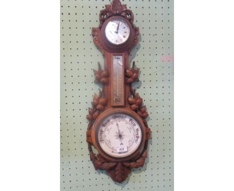 An Edwardian black forest-type wheel barometer, having primary ceramic dial beneath brass thermometer and clock surmount, the
