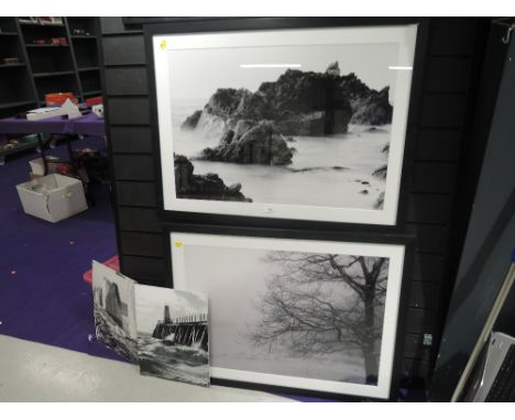 A photographic print of shore line and rock formation in black frame with similar tree in mist scene