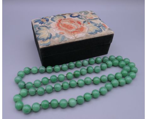 A vintage Chinese box covered with silk embroidery containing a string of jade beads. The box 13.5 cm wide.