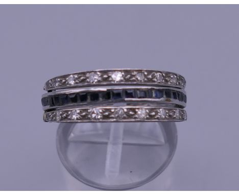 An unmarked white gold diamond, ruby and sapphire three-part ring. Ring size N. 5.1 grammes total weight.  