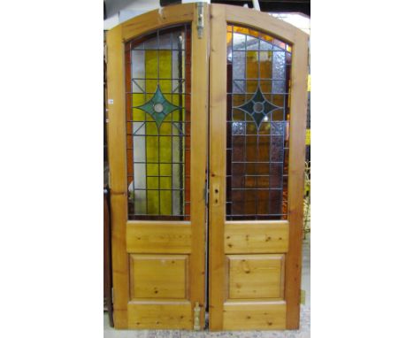 A pair of stripped and waxed pine internal doors of arched form with Victorian style leaded light panels and brass fittings, 