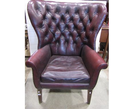 An upholstered button back library chair with scrolled arms, maroon leather finish, on square taper legs