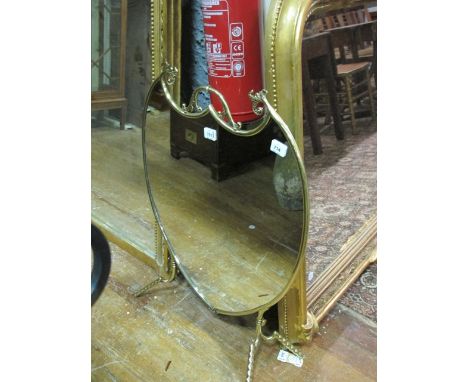 A BRASS AND MIRRORED FIRESCREEN of shield shaped outline with carrying handle raised on splayed legs 77cm (h) x 60cm (w)