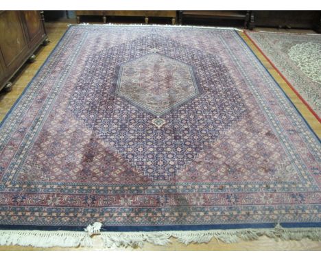 A WOOL RUG the light pink and indigo ground with central floral panel within a conforming border 358cm x 275cm