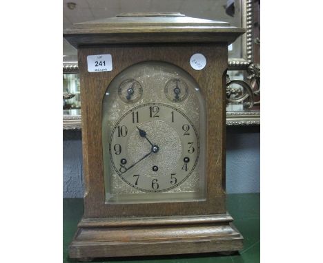 AN OAK CASE BRACKET CLOCK the domed hood above an arched door containing a silvered dial raised on a moulded base with bun fe