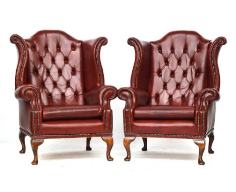 A pair of oxblood leather button upholstered wingback armchairs of recent manufacture, on cabriole legs, each 87cmW 