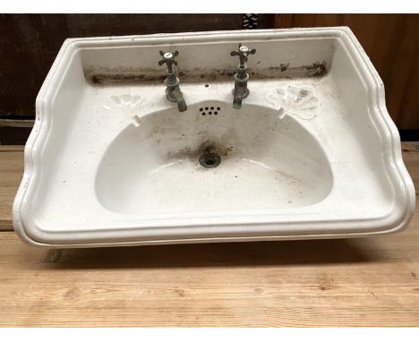 An early 20th century wash basin, with brass taps and plughole, with cast metal wall mount (af), 66x45cmProvenance: Bryanston